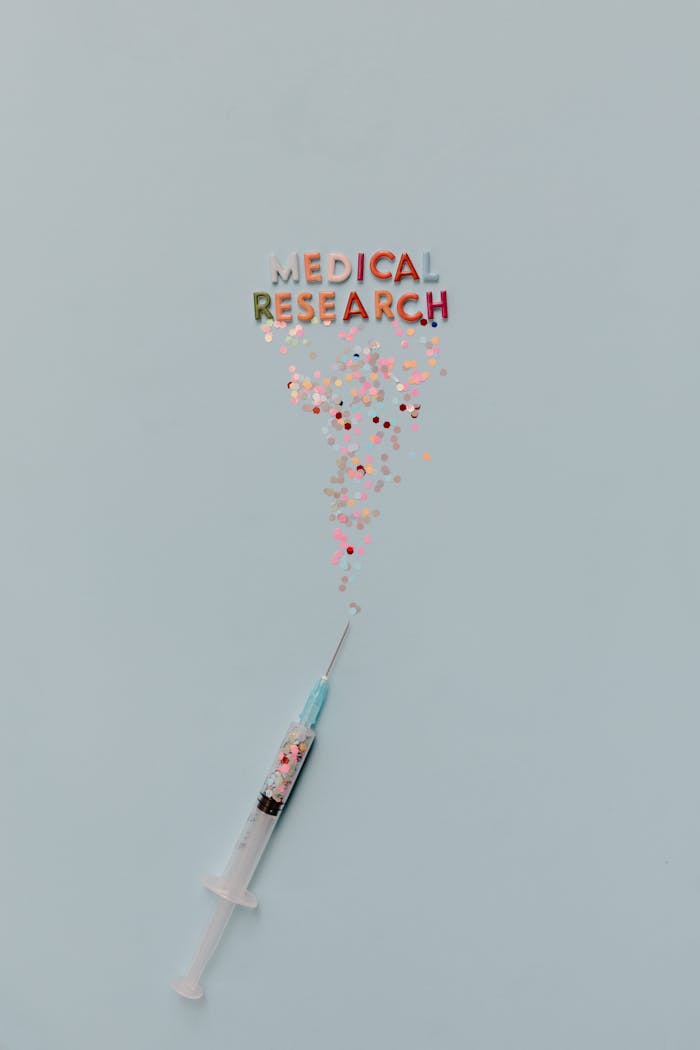 Syringe releasing confetti with 'MEDICAL RESEARCH' text on a blue background.